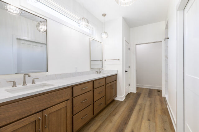 Spacious custom primary bathroom with a double vanity, quartz countertops, natural oak cabinetry, oversized mirrors, luxury vinyl plank flooring, and brushed nickel fixtures in a Columbia City, Indiana custom home by Wannemacher Design Build.