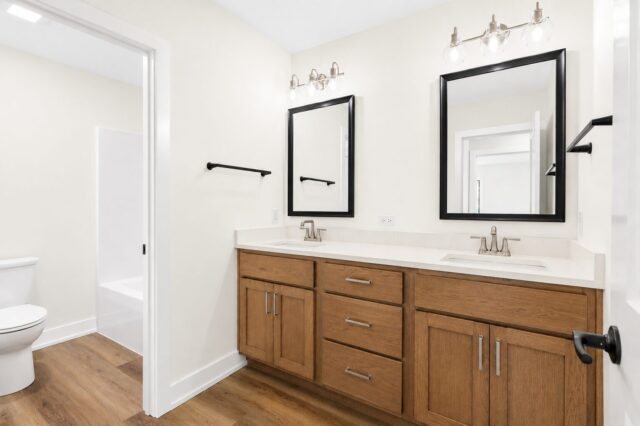 Custom bathroom with a double vanity, quartz countertop, oak cabinetry, black framed mirrors, brushed nickel fixtures, and Sherwin-Williams Alabaster walls by Wannemacher Design Build in Columbia City, Indiana.