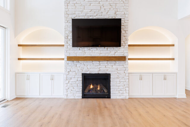 Floor-to-ceiling stone fireplace with gas insert, floating wood mantel, and built-in cabinetry in a custom Fort Wayne home.