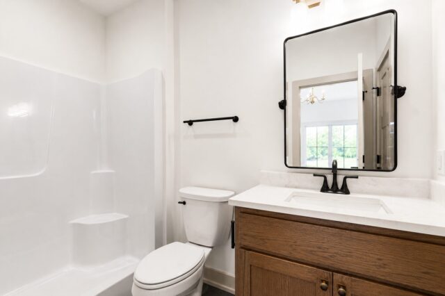 Modern guest bathroom featuring a quartz vanity, wood cabinetry, matte black fixtures, black framed mirror, and tub shower combination in a custom home in Decatur, Indiana.
