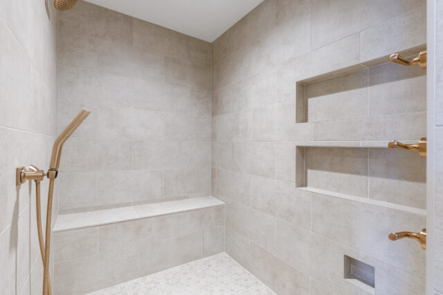 Walk-in tiled shower with built-in bench, recessed wall niches, and brushed brass fixtures in a Northeast Indiana custom home.