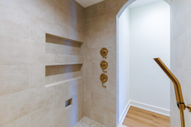 Custom tiled shower with multiple control valves, recessed niches, and brass fixtures in a Northeast Indiana home.