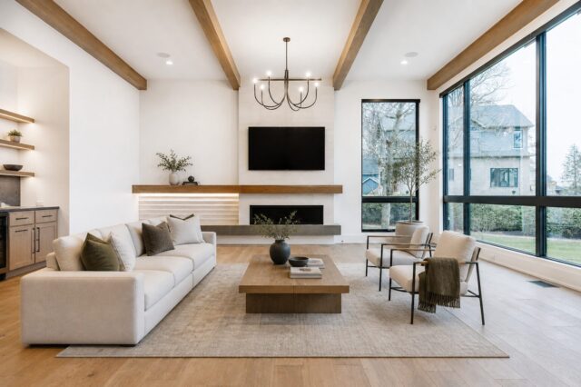 Modern custom living room at the Lake George home by Wannemacher Design Build featuring exposed wood beams, floor-to-ceiling windows, and a contemporary fireplace.