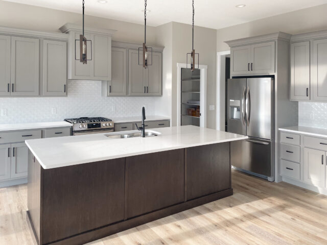 Custom kitchen with large quartz island, pendant lighting, gray cabinetry, and stainless appliances by Wannemacher Design Build in Fort Wayne Indiana.