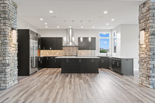 Modern kitchen with large center island, custom dark cabinetry, stainless steel appliances, and stone column accents in a custom home by Wannemacher Design Build in Fort Wayne, Indiana.