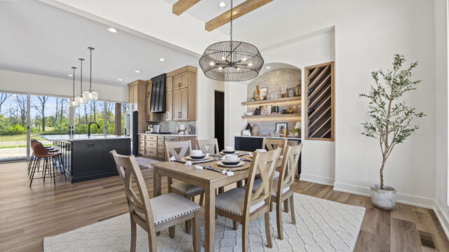Open-concept dining room and kitchen with wood cabinetry, black island, pendant lighting, and large windows in a custom home by Wannemacher Design Build in Fort Wayne, Indiana.