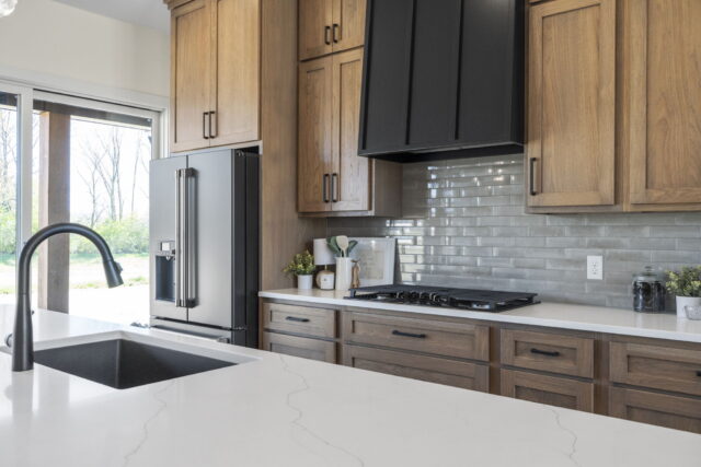 Custom kitchen with natural wood cabinetry, quartz countertops, stainless steel refrigerator, and modern black range hood in a Wannemacher Design Build home in Decatur, Indiana.