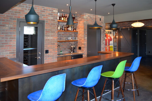 Custom basement bar with exposed brick walls, walnut countertop, pendant lighting, and modern upholstered bar stools.