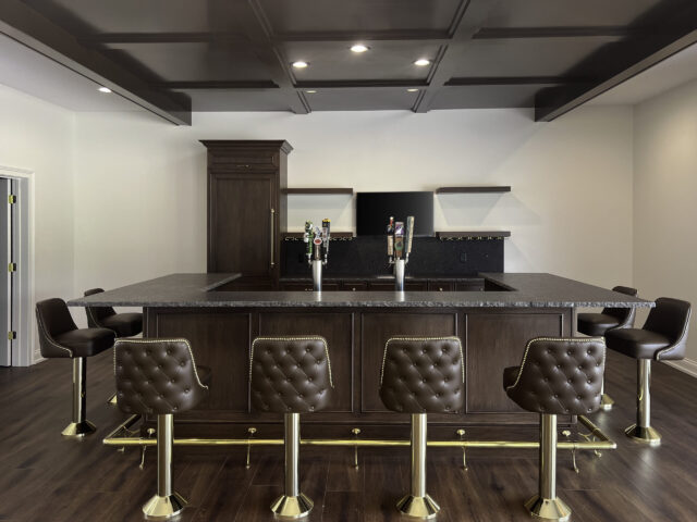 Finished bar featuring rich wood cabinetry, coffered ceiling detail, granite countertop, and leather seating, and beer taps.