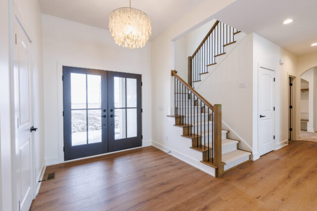 Entryway with wood staircase, black iron railing, and double glass front doors in a Northeast Indiana custom home.